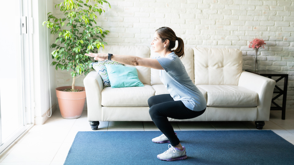 Full length view of an active woman in her 40s working out and doing some squats at home